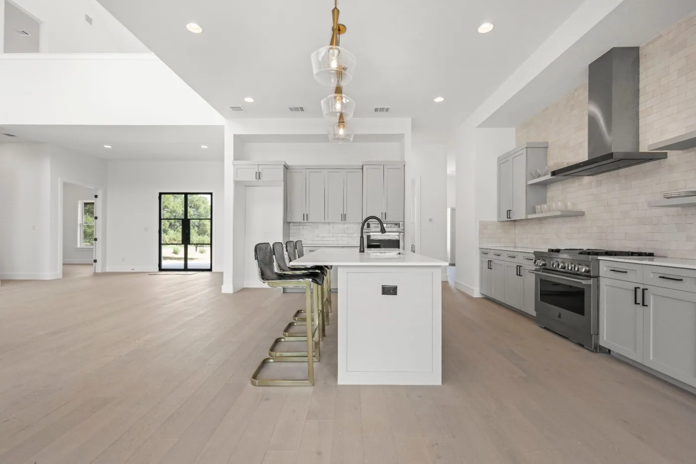 Open-concept kitchen with a wood range hood opening to the living and dining areas in the Chipshot custom home by Atlas Custom Homes in Texas Hill Country