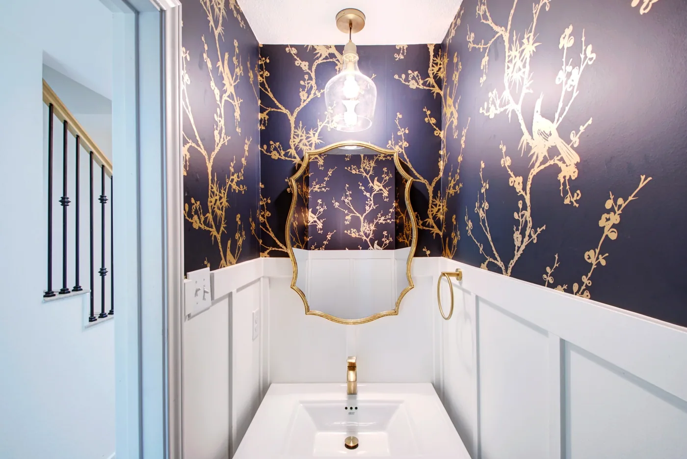 Remodeled powder room with blue and gold wallpaper and white wainscoting