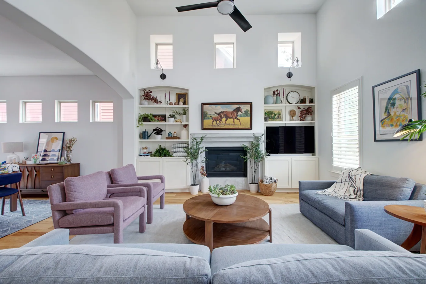 Bright livingroom with stone fireplace, blue couches, and purple chairs