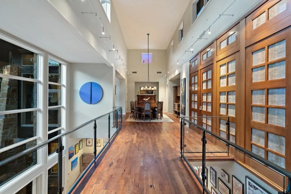 Interior view of a two-story hallway with a wooden floor and large doors on one side.